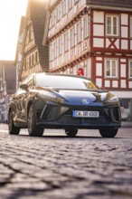 Black car in a half-timbered town, street view, morning light, MG4 electric car, deer e-car