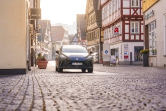 Black car in an old town with shops and cobblestone streets, MG4 electric car, deer e-car sharing,
