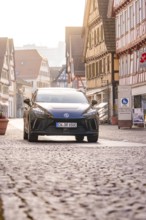 Black car drives through an old town with half-timbered houses and cobblestones, MG4 electric car,