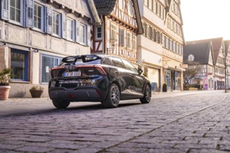 Car standing in front of half-timbered houses in a paved old town street under soft light, MG4