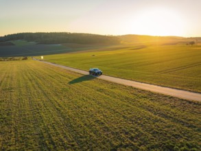 Small car on a country road surrounded by vast fields and an impressive sunset, MG4 electric car,