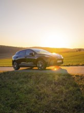 Black car parked on a country road surrounded by green fields when the sun is low, MG4 electric