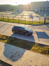 Black car driving on a paved road surrounded by a modern building landscape at sunset, MG4 electric