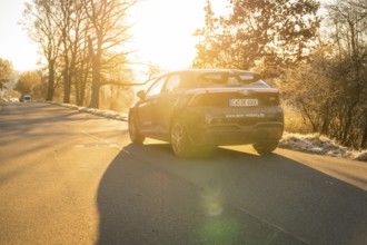 Car moving on a quiet path surrounded by trees at sunset, MG4 electric car, Deer e-Carsharing,