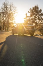 Car drives on a road under a dramatic sunset, casts long shadows, MG4 electric car, deer e-car