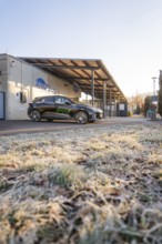 Parked electric car in front of a building on frosty ground on a clear winter morning, MG4 electric