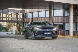 Black car on an urban road in front of a modern building at sunset, MG4 electric car, Deer