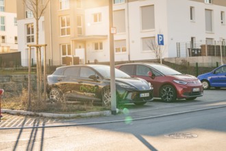 Two electric cars in a parking lot in front of residential buildings, in the warm light of the