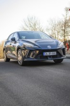 Car drives across tree-lined road, modern design reflected in sunshine, MG4 electric car, deer