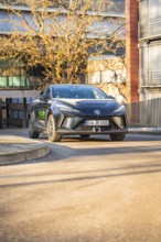 Black car drives on a curved road past an architecturally designed building, MG4 electric car, Deer