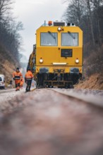 Close-up of a yellow train with workers on rails under cloudy sky, using a tamping machine on the