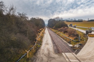 Construction site along a rail line surrounded by bare autumn forest, tamping machine used on the