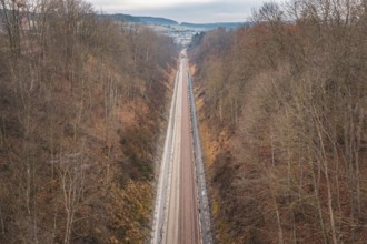 Rail line snakes through hilly autumn landscape with bare trees, using a tamping machine at the