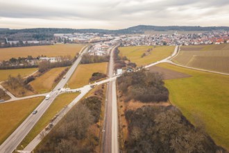Wide fields and village settlement along a railway line under cloudy sky, tamping machine used at