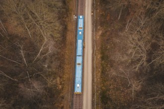 Bird's-eye view of railway line with yellow train in a wooded region, using a tamping machine at