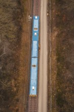Aerial view of a yellow train on a construction site in a wooded area, using a tamping machine at