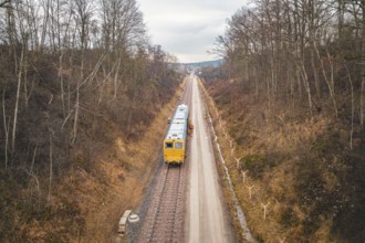 Train travels through a wintry landscape with bare trees along the tracks, using a tamping machine