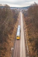 Yellow train on rails in an autumn landscape with a view of a distant city, using a tamping machine