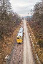 Yellow train during construction on a long rail line surrounded by bare trees, using a tamping