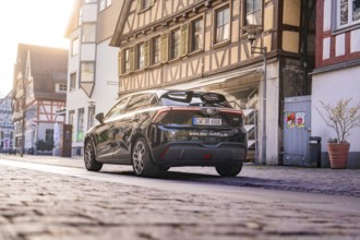 Black car from behind in a street with historic half-timbered houses in daylight, MG4 electric car,