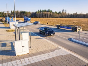 A car turns onto a wide road surrounded by parked vehicles and fields, MG4 electric car, Deer E-