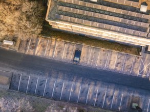 Aerial view of a parking lot with a single car, next to a building with solar panels, MG4 electric