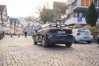 Car parked on paved street in an old town, half-timbered houses in the background, MG4 electric