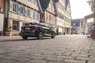 Car drives quietly through a street with traditional architecture and half-timbered houses, MG4
