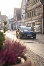 Black car parked on a paved street in a historic town with half-timbered houses in daylight, MG4