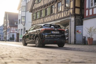 Rear view of a black car in front of historic half-timbered houses, captured in the evening mood,