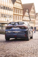 A modern car drives on a cobblestone street in front of half-timbered houses in the old town, MG4