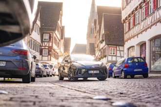 A modern car on a paved street in the old town, surrounded by half-timbered houses and parked cars,