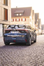 A modern car is parked on a cobblestone street in an old town at sunset, MG4 electric car, deer