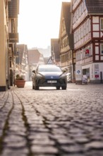 Cobblestone street with a car surrounded by half-timbered houses in glowing sunlight, MG4 electric