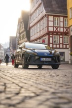 Black car on a busy paved road between half-timbered houses in an urban scene, MG4 electric car,