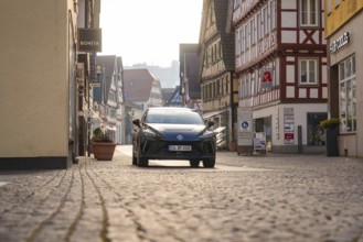 Black car in an inner city street with half-timbered houses, surrounded by a busy atmosphere in