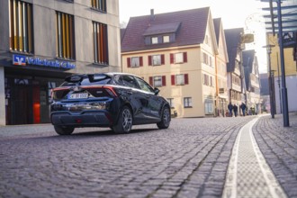 A car drives through a city street flanked by traditional buildings and empty roads, MG4 electric