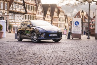 A car is parked in a historic old town with half-timbered houses and a charming atmosphere, MG4