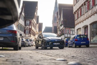 Car in a narrow old town street with half-timbered houses and church in the background, MG4