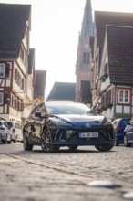 A car in a paved old town street with church and half-timbered houses, MG4 electric car, Deer