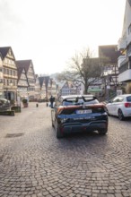 Black car on a paved road between historic half-timbered houses, MG4 electric car, Deer