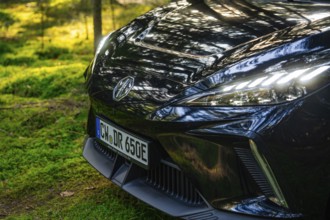 Close-up of front lights of a car with reflecting sunlight in the forest, MG4 electric car, Deer