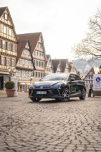 Car parked in a picturesque old town with half-timbered houses and paved streets, MG4 electric car,
