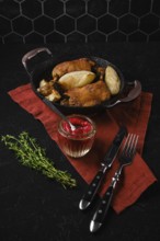 Roasted duck legs in a skillet next to pears and a small jar of lingonberry sauce. Fresh thyme is