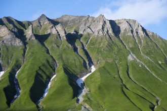 Steep green mountain ridges rise up under a blue sky, mountainous landscape between Gudauri and the