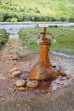 A rusty water spring over stones in front of a green landscape, mineral spring near Nadibani, White