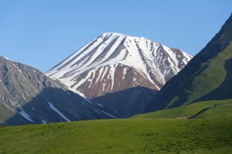 Snowy mountain with shadows cast over green hills, landscape between Kvesheti and Gudauri,