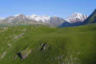 Green wide meadow against a mountain backdrop with snow, landscape between Kvesheti and Gudauri,