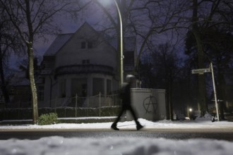 A person walks past a dark villa with an anarchy symbol written on the wall during the large-scale