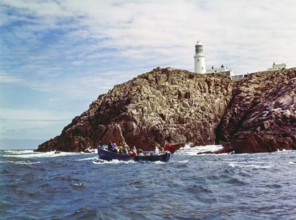 Tour boat passing rocky cliffs at Round Island lighthouse, Isles of Scilly, Cornwall, England, UK